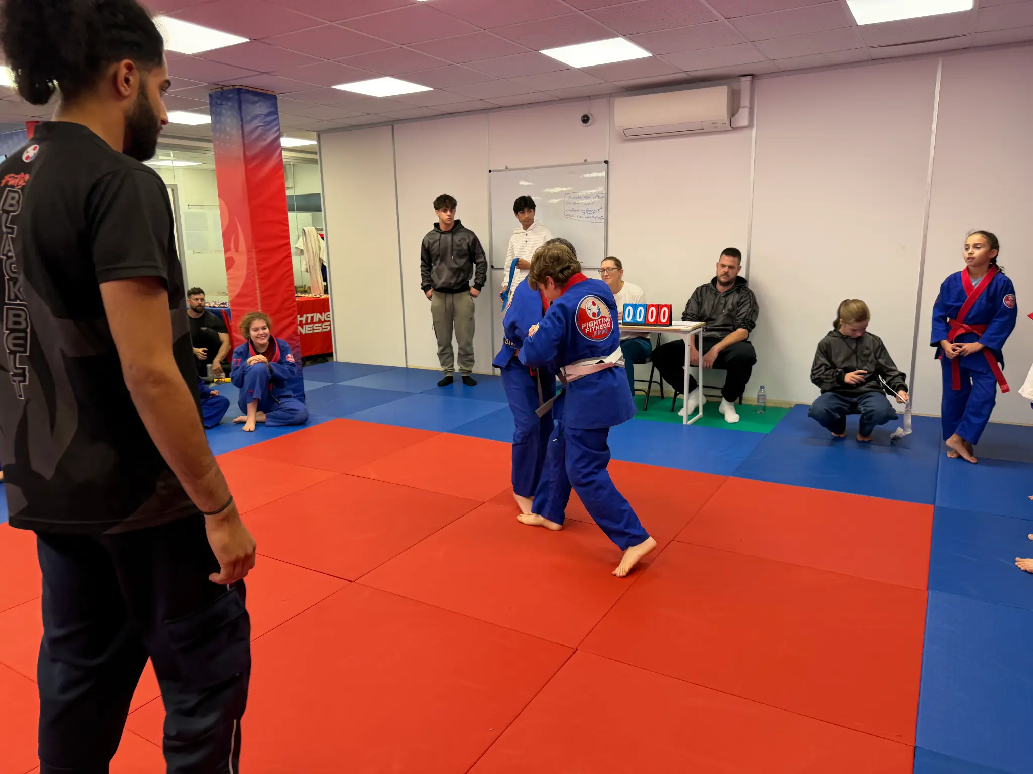 Two young judoka competing as families watch and cheer