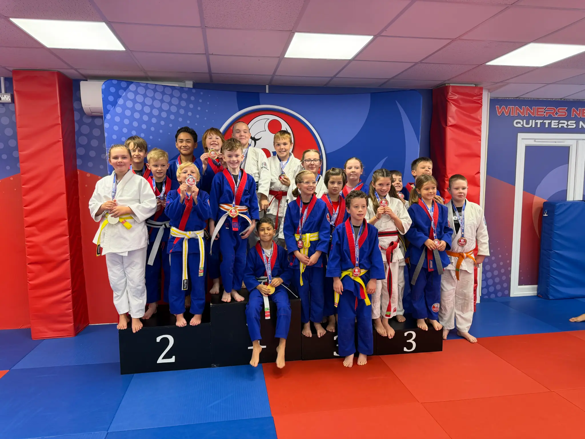 A Team Festival group celebrating in front of the Fighting Fitness Judo wall